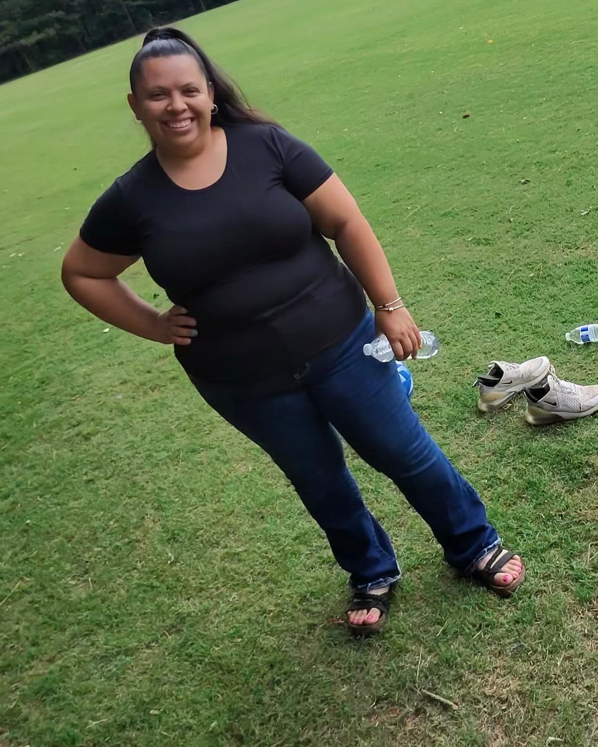 Sofia Cortes at a soccer field, holding water bottles, with cleats on the grass beside her